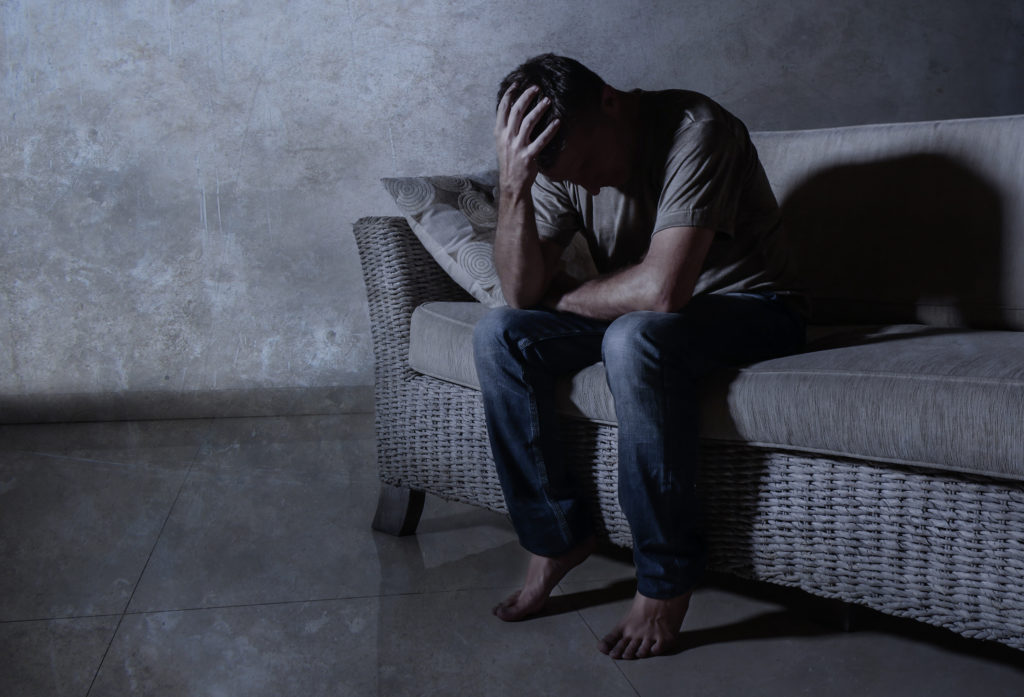 stressed man sitting on couch alone in the dark